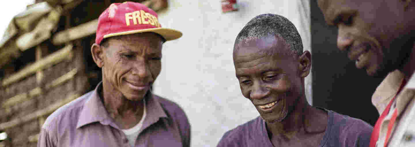 Three smiling African men studying a document with information about a missing family member.