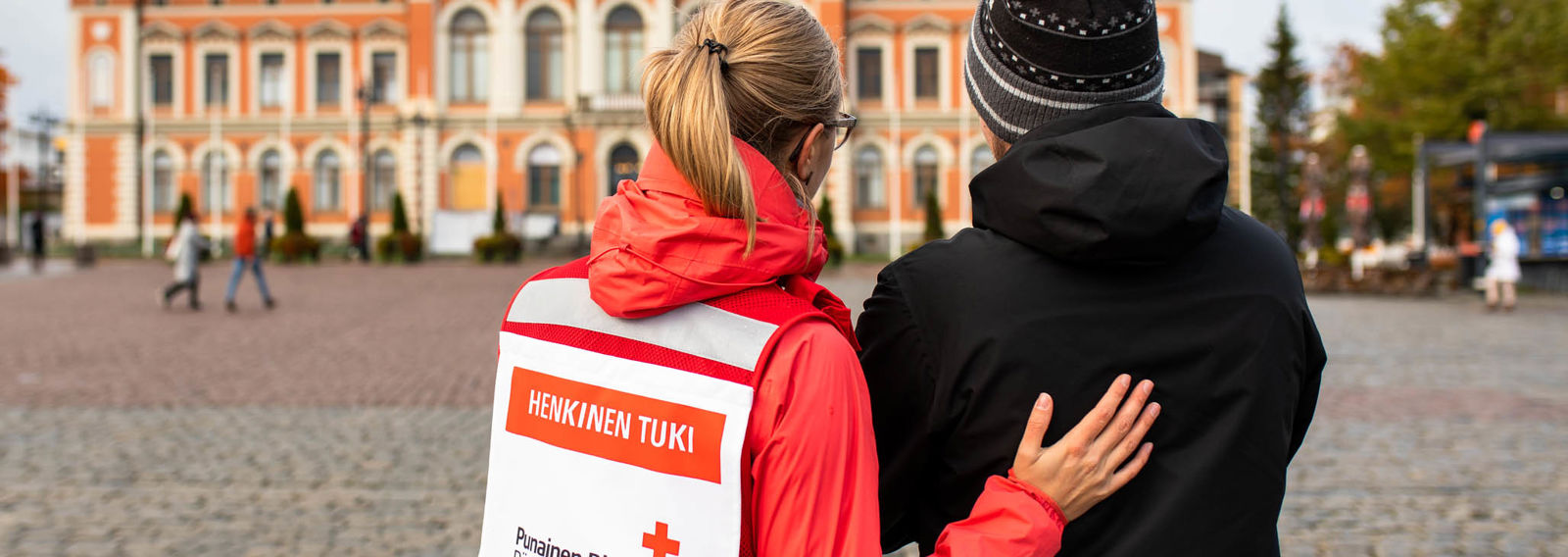 A woman wearing a Red Cross volunteer vest and talking to a shaken man in the Kuopio Market Square.