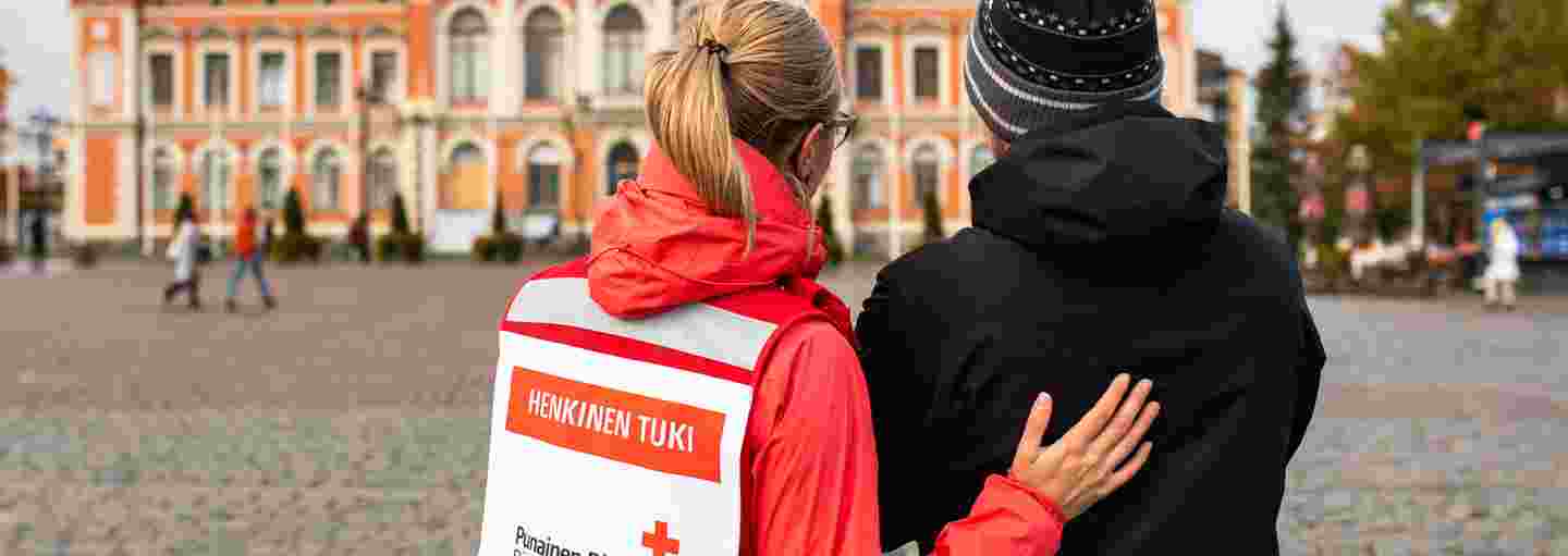 A woman wearing a Red Cross volunteer vest and talking to a shaken man in the Kuopio Market Square.