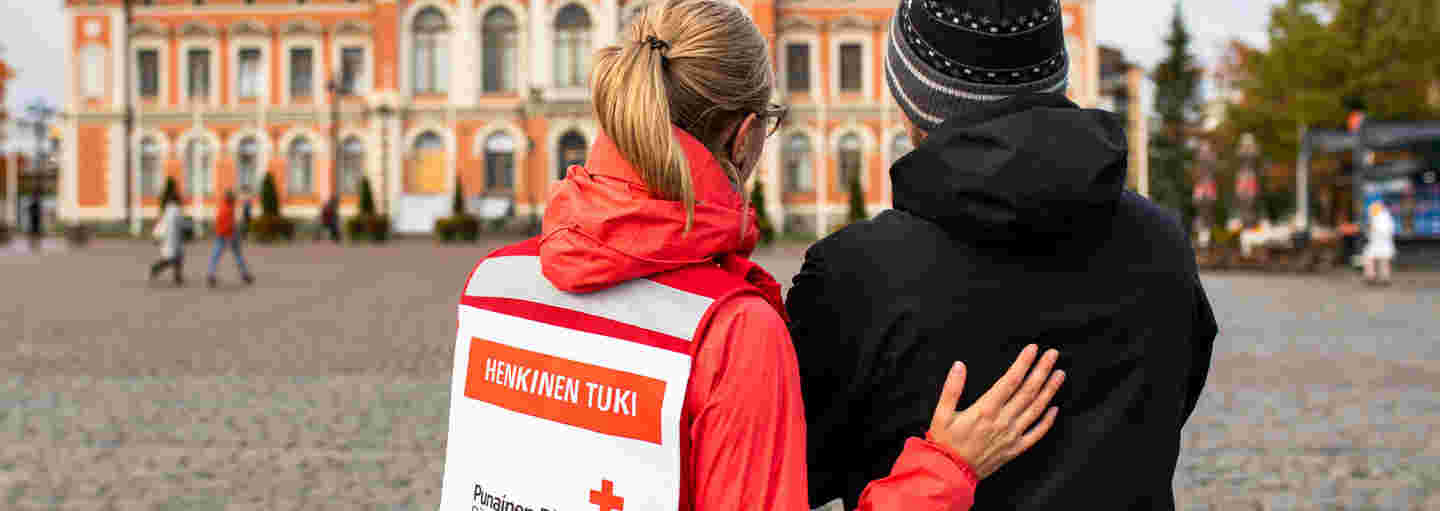 A woman wearing a Red Cross volunteer vest and talking to a shaken man in the Kuopio Market Square.