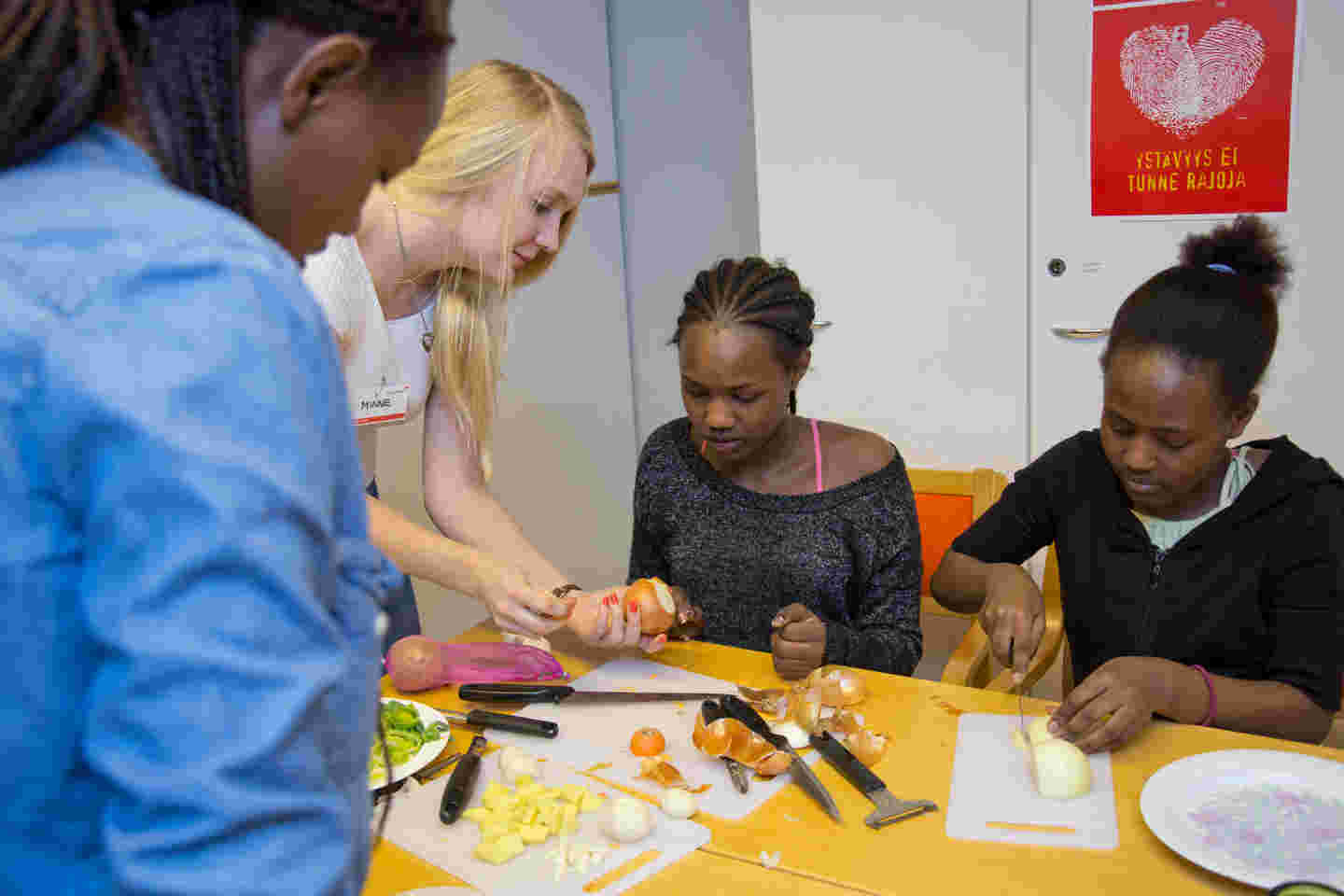 Three immigrant women cooking together with a Red Cross volunteer.