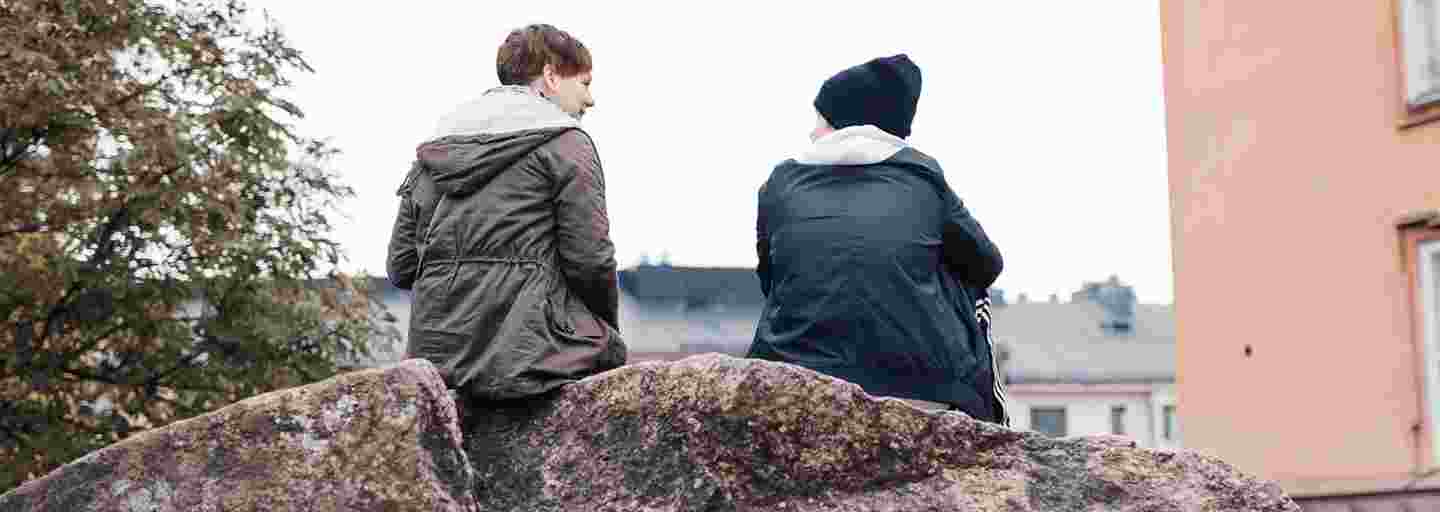Two young adults chatting and sitting on a rock in an autumn landscape.