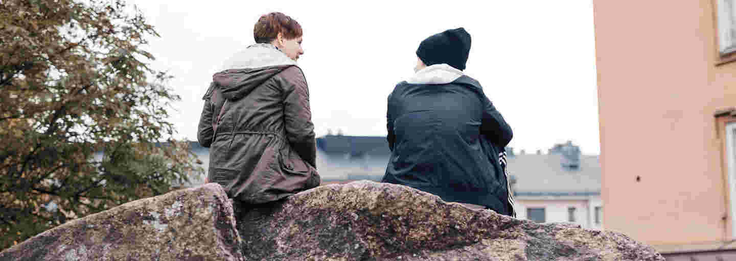 Two young adults chatting and sitting on a rock in an autumn landscape.