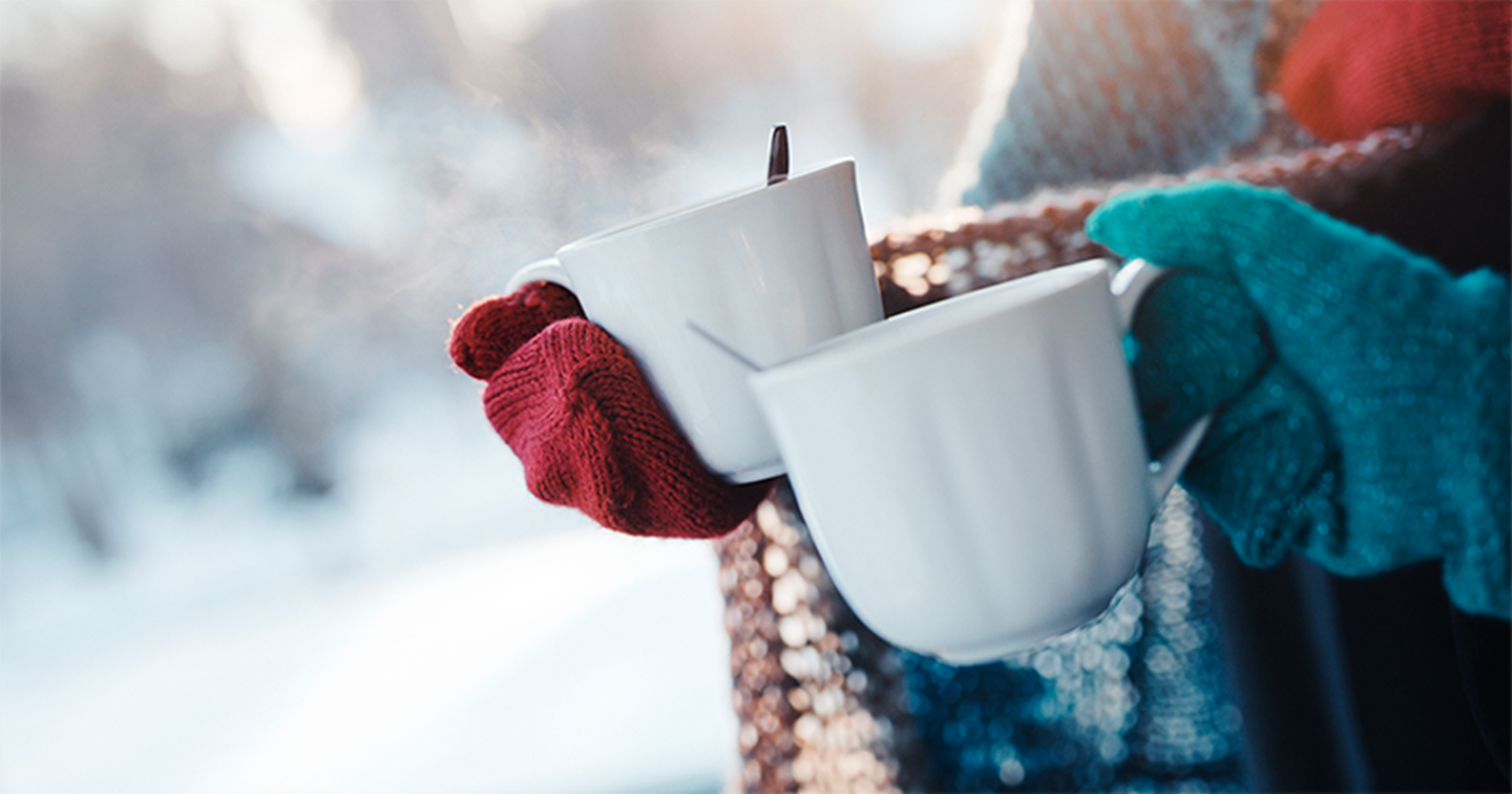Two people holding steaming drinking cups outside in the winter weather.
