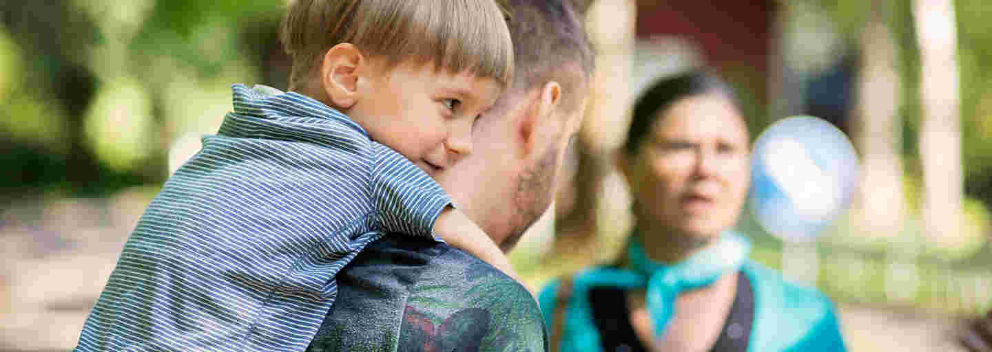 A father giving a piggyback ride to a small boy and a woman facing the camera standing opposite them.