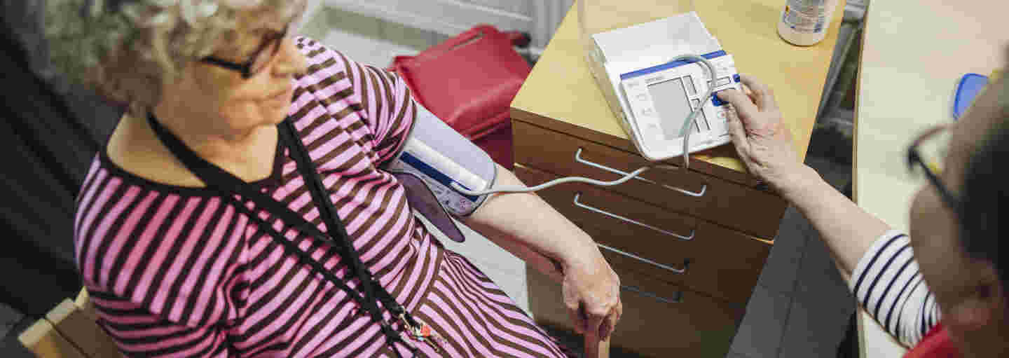 A woman wearing a Red Cross volunteer vest taking the blood pressure of an elderly woman.