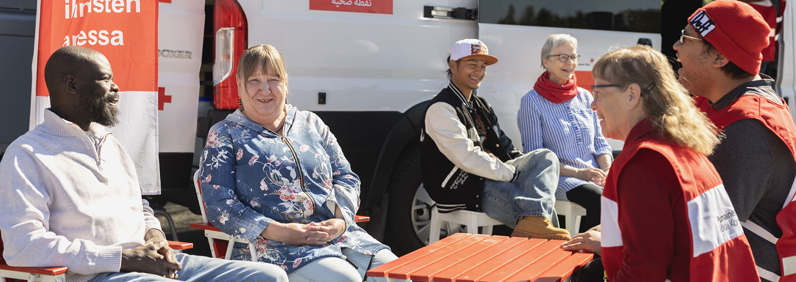 A group of people sit discussing at a mobile Red Cross Health Point.