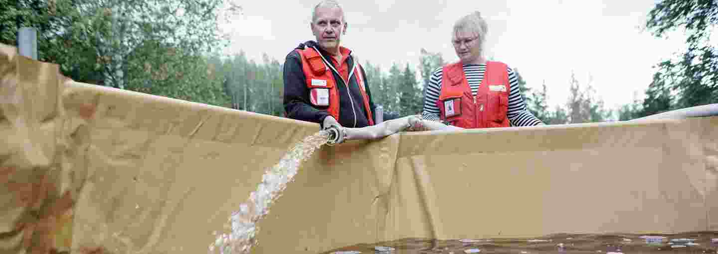 A woman and a man wearing Red Cross uniforms filling a pool with clean water.