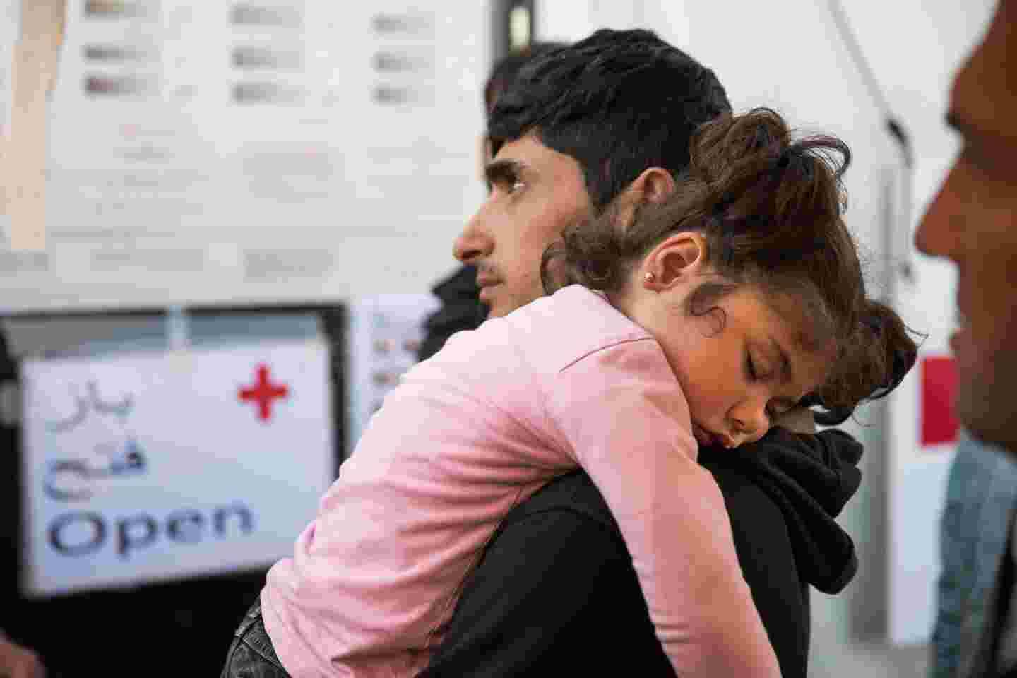 A small girl sleeping against her father’s shoulder at a Red Cross office where they have come for help.