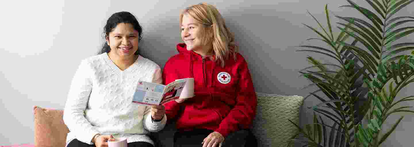 Two smiling girls sitting on a sofa reading a Red Cross brochure.