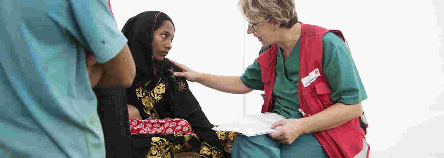 A young Bangladeshi woman is talking to a Red Cross aid worker at a field hospital.