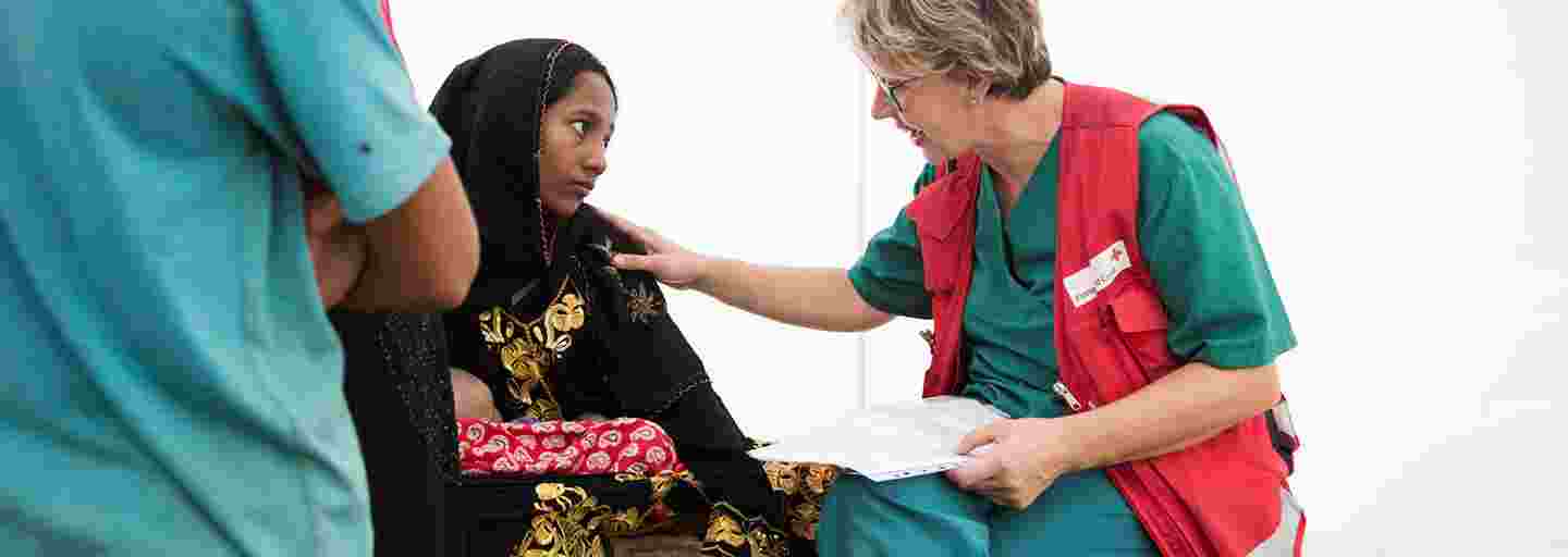 A young Bangladeshi woman is talking to a Red Cross aid worker at a field hospital.