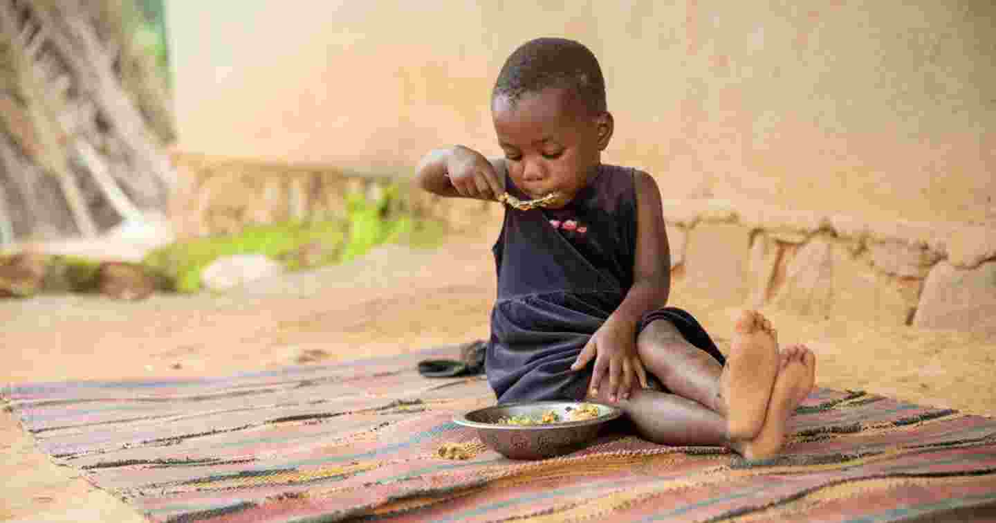 A small child sitting on the ground, eating.