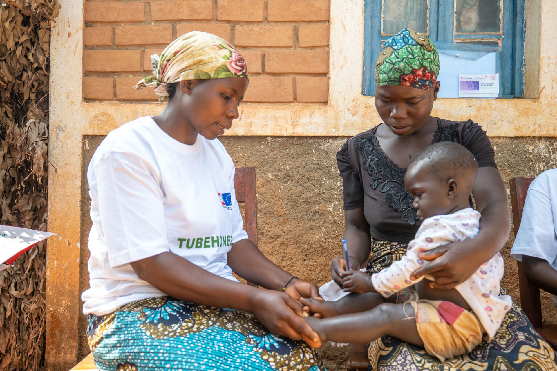 A woman examining a baby held by its mother.