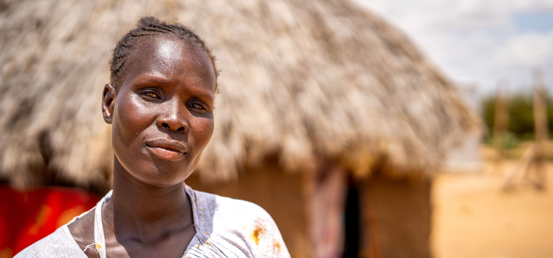 A woman looks directly into the camera, with a building behind her. 