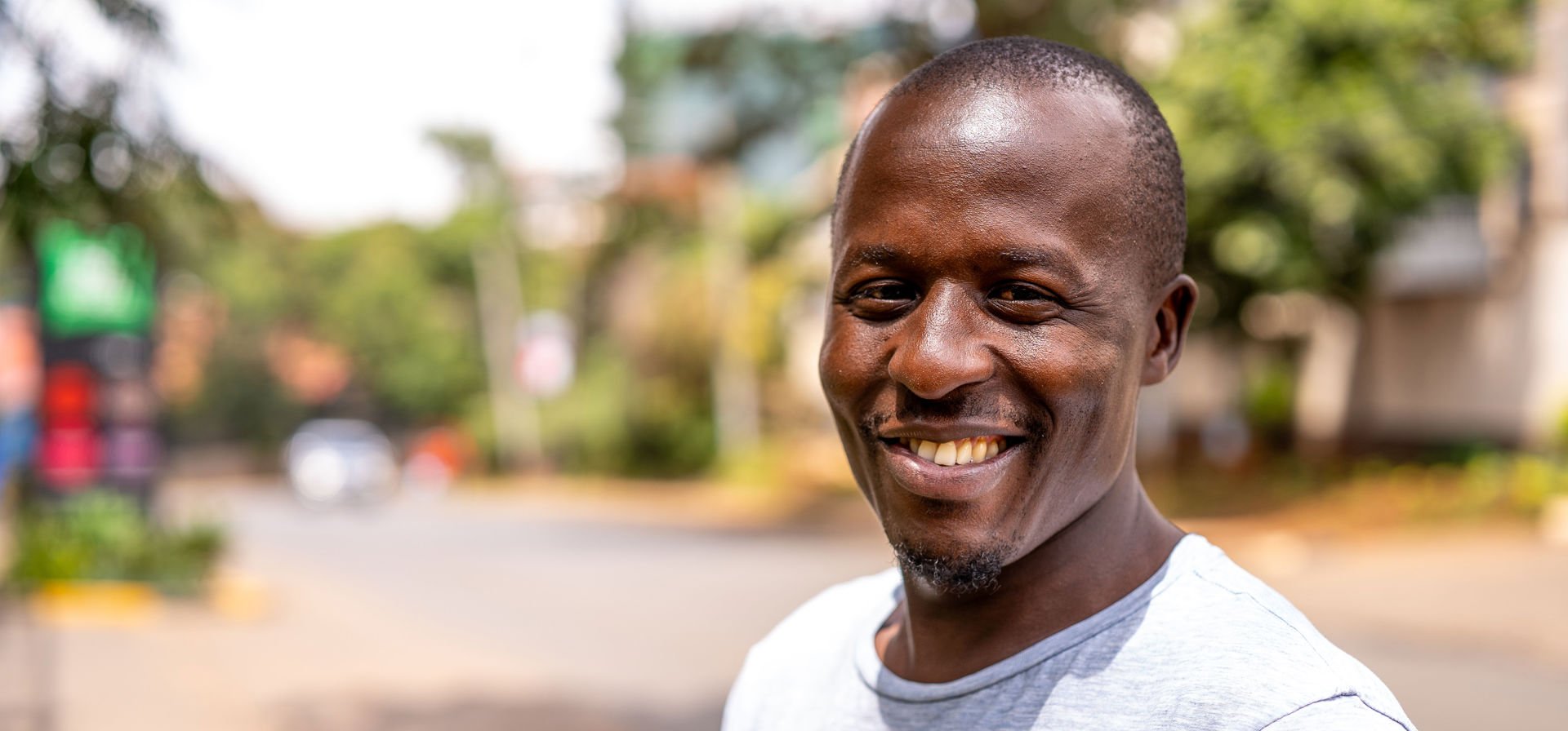 A man looks into the camera, with a street view of Nairobi behind him.