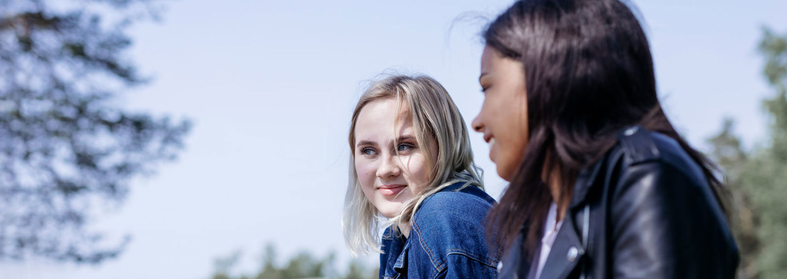 Two smiling young women talking outside in the sun.