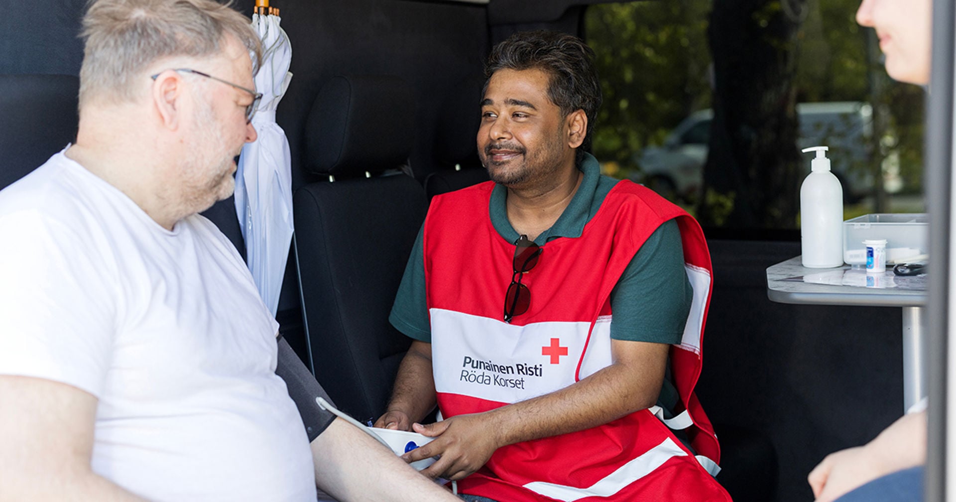 A Health promotion volunteer is measuring the blood pressure of a person sitting beside him.