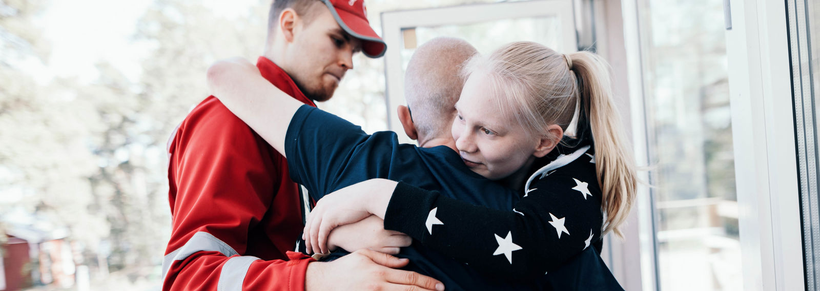 A smiling child hugs their father. A nearby Red Cross volunteer provides support to the father.
