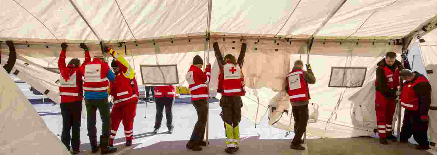 Seven people in Red Cross gear putting up a tent.