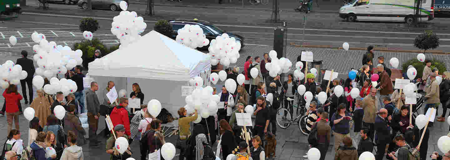 Dozens of people holding balloons in an anti-racism event in a market square.