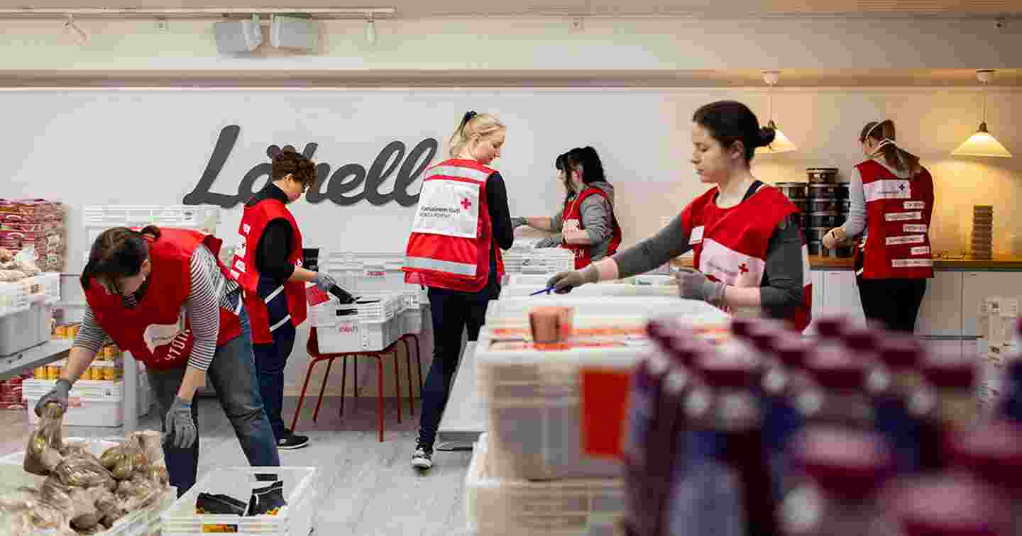 Six people in Red Cross volunteer vests arranging food packages.