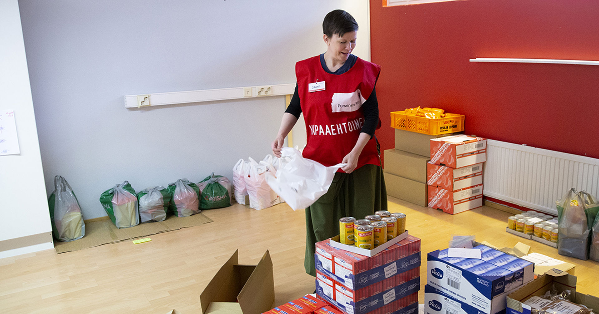 A person in a Red Cross volunteer vest is packing groceries with a smile.