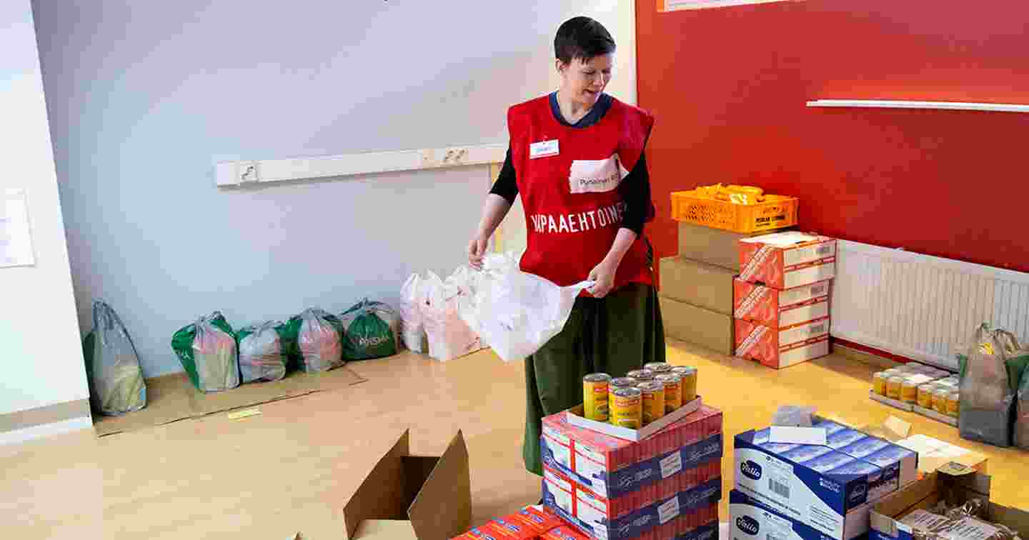 A person in a Red Cross volunteer vest is packing groceries with a smile.