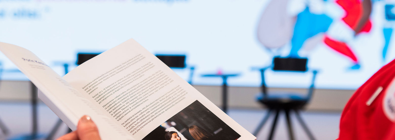 A person wearing a Red Cross hoodie is browsing a brochure in their hand. 